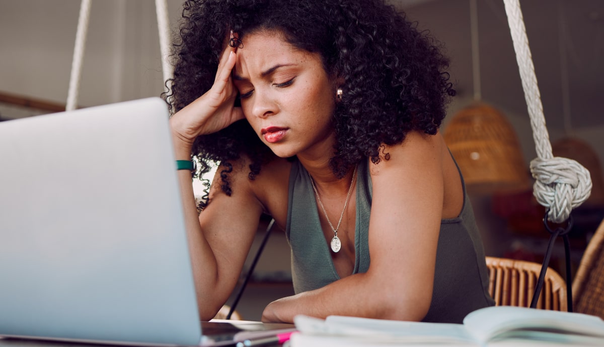 An exhausted woman sitting in front of a computer with her head in her hands, showing signs of burnout such as fatigue and stress.