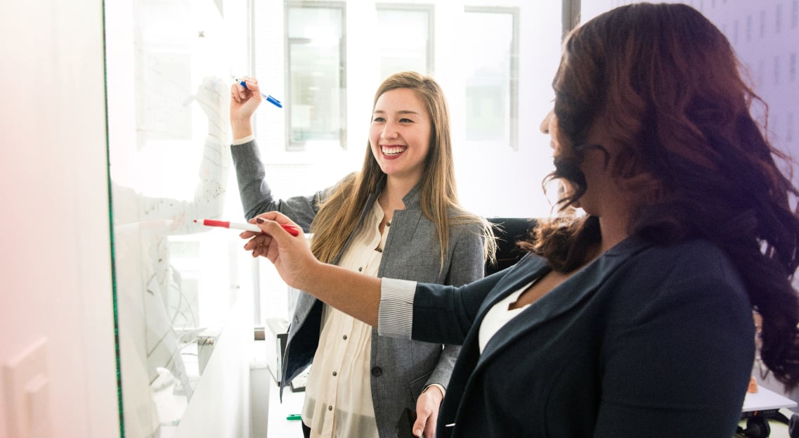 Two coworkers discuss a project in front of whiteboard.