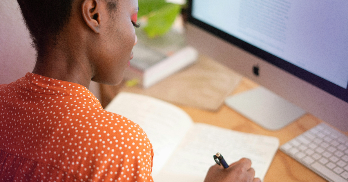 A person making notes on paper, sitting in front of a computer.